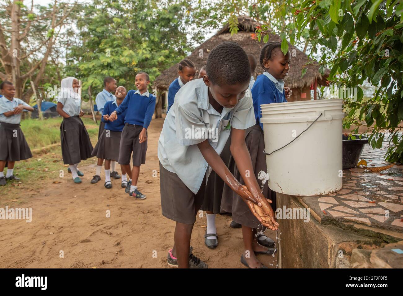 Dodoma, Tansania. 08-18-2019. Ein afrikanischer Junge wascht sich die Hände, während andere Studenten Spaß haben, während sie in der Schlange auf ihre Reihe warten. Stockfoto