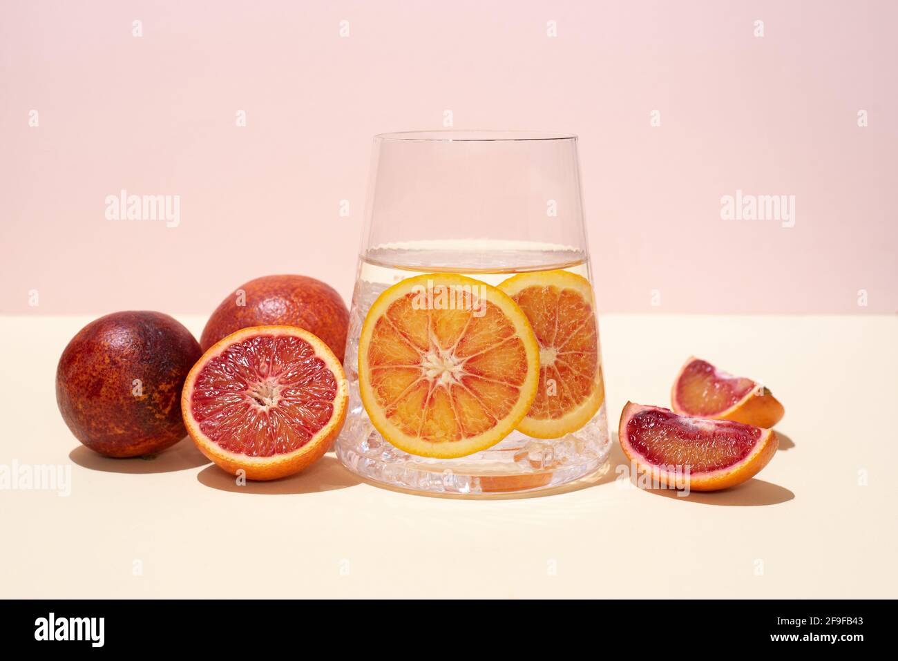 Glas mit funktionellem Wasser und Scheiben von Zitrusfrüchten und Blutorangen auf gelb-rosa Hintergrund, gesunde Getränke, Nahaufnahme. Stockfoto
