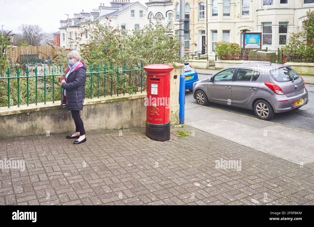 Eine ältere Frau, die während des vor einem Postamt Schlange steht Covid mal mit neu bemalten George VI Briefkasten draußen Stockfoto