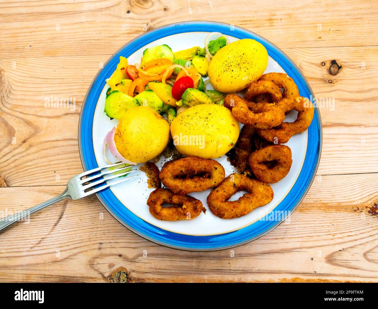 Mittagessen Calamari Ringe in knusprig gewürzten Teig Salz und Pfeffer Tintenfisch mit neuen Kartoffeln und Salat mit blauem Rand Weißer Teller auf einer Holzplatte Stockfoto
