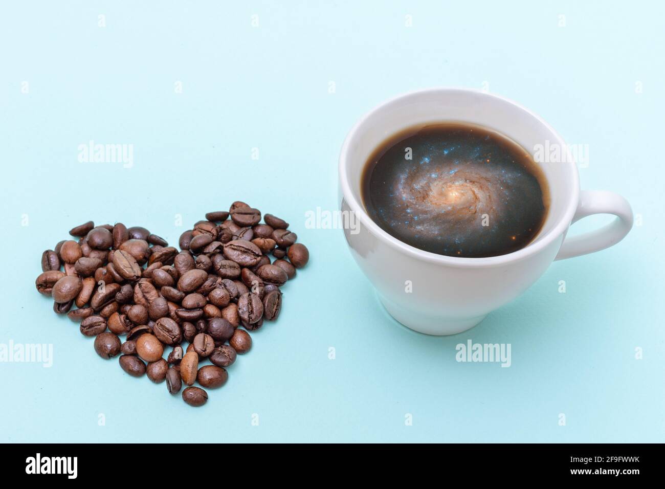 Tasse schwarzen Kaffee mit Schaumstoff in Form einer Galaxie, Kaffeekörner in Form eines Herzens auf blauem Hintergrund. Morgenkaffee für die Liebsten. Spac Stockfoto