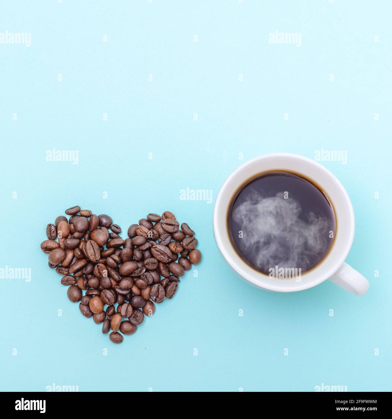 Tasse dampfenden heißen schwarzen Kaffee und Körner Kaffee in Form eines Herzens auf blauem Hintergrund, Kopierfläche, Draufsicht, quadratische Form. Kaffee am Morgen Stockfoto