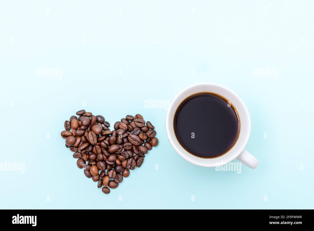 Tasse heißen schwarzen Kaffee und Körner Kaffee in Form eines Herzens auf blauem Hintergrund, Kopierraum, Draufsicht. Morgenkaffee für die Liebsten Stockfoto