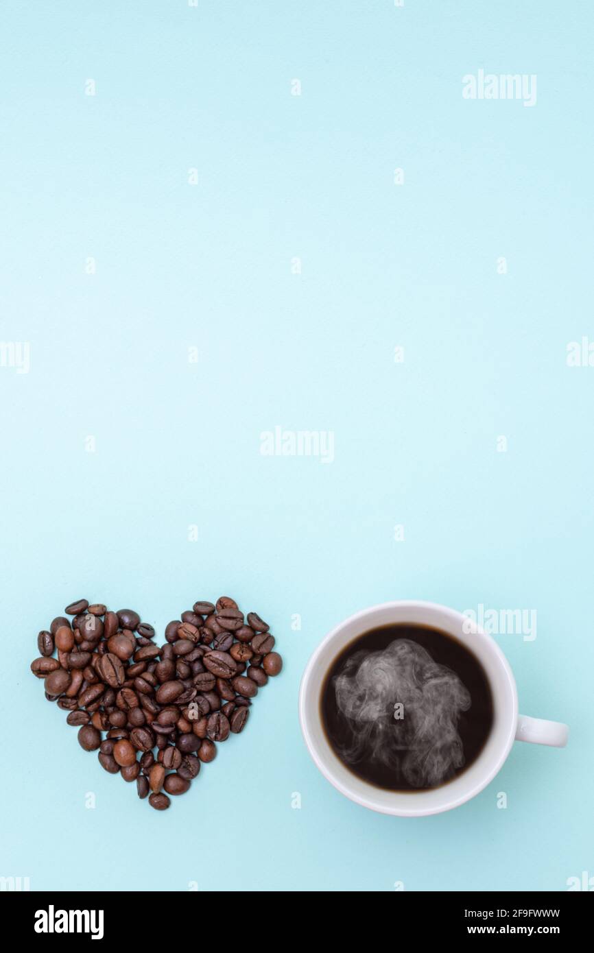 Tasse dampfenden heißen schwarzen Kaffee und Körner Kaffee in Form eines Herzens auf blauem Hintergrund, Kopierfläche, Draufsicht, vertikale Form. Morgencoff Stockfoto