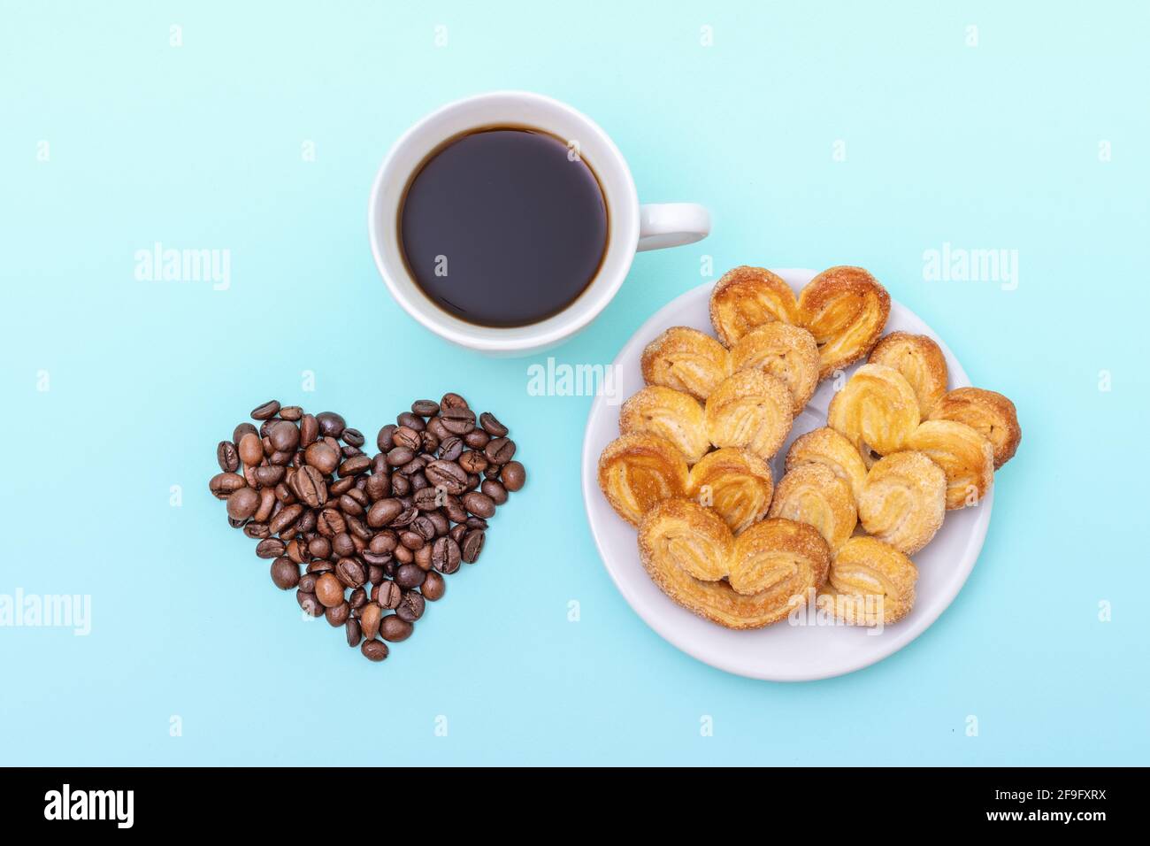 Tasse schwarzen Kaffee, Kekse in Form von Herzen, Körner von Kaffee in Form eines Herzens auf blauem Hintergrund, Kopierraum, Draufsicht. Morgencoff Stockfoto