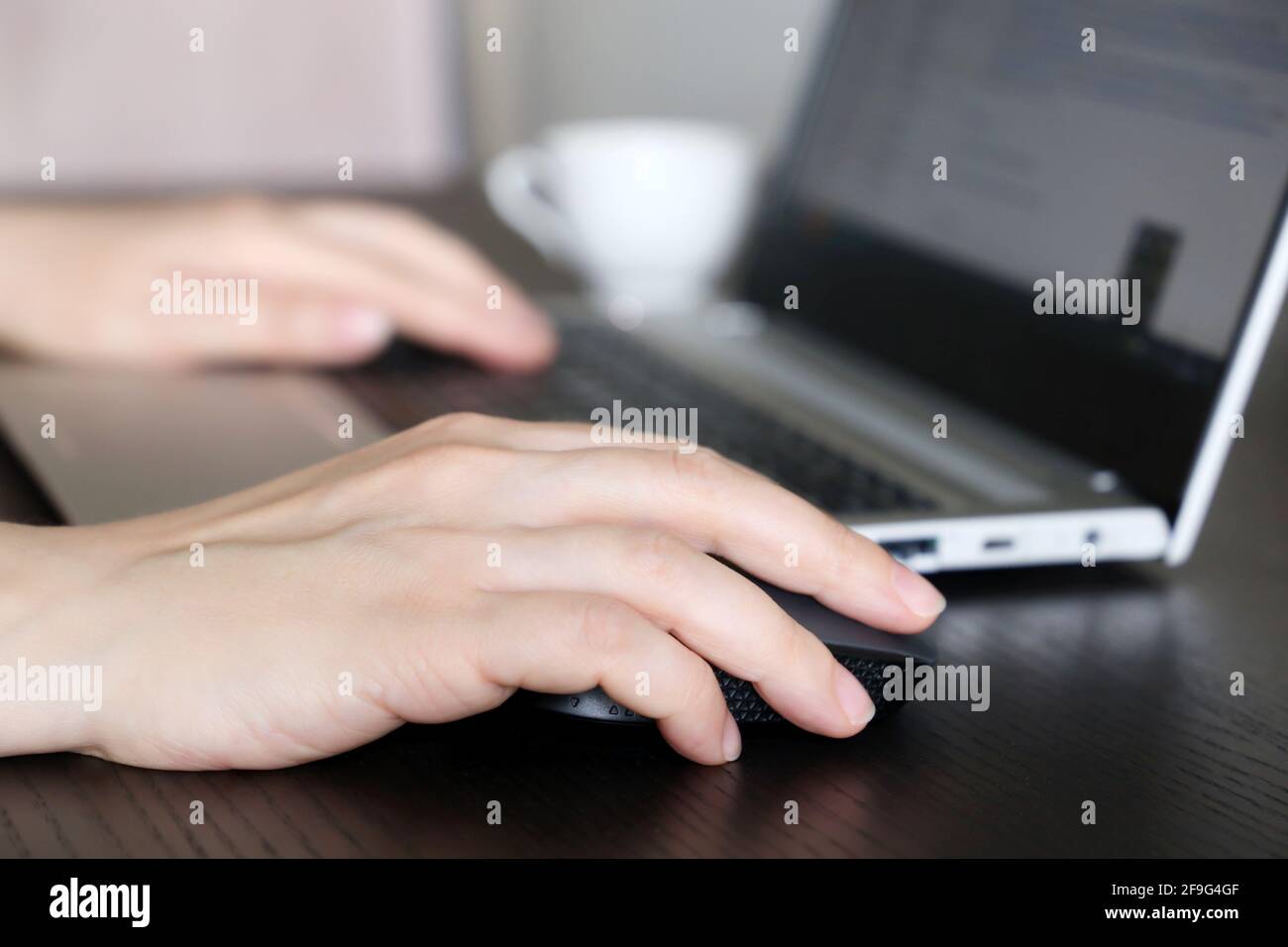 Weibliche Hände auf Laptop-Tastatur und Computer-Maus. Frau arbeitet mit Docs, die am Holztisch sitzen Stockfoto
