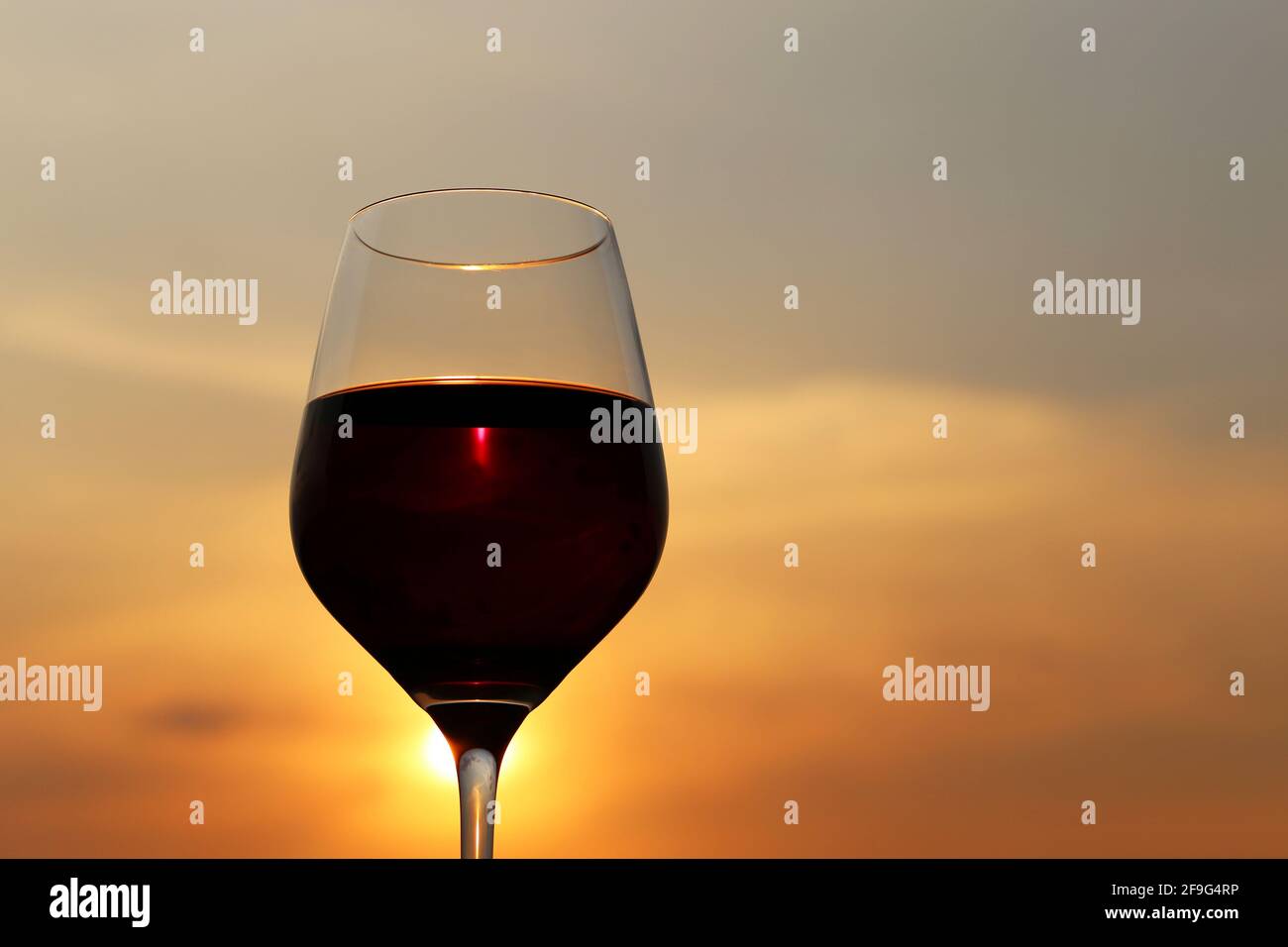 Glas mit Rotwein auf Sonnenuntergang Hintergrund, Abendsonne scheint durch das Glas. Konzept der Feier, Weinindustrie Stockfoto