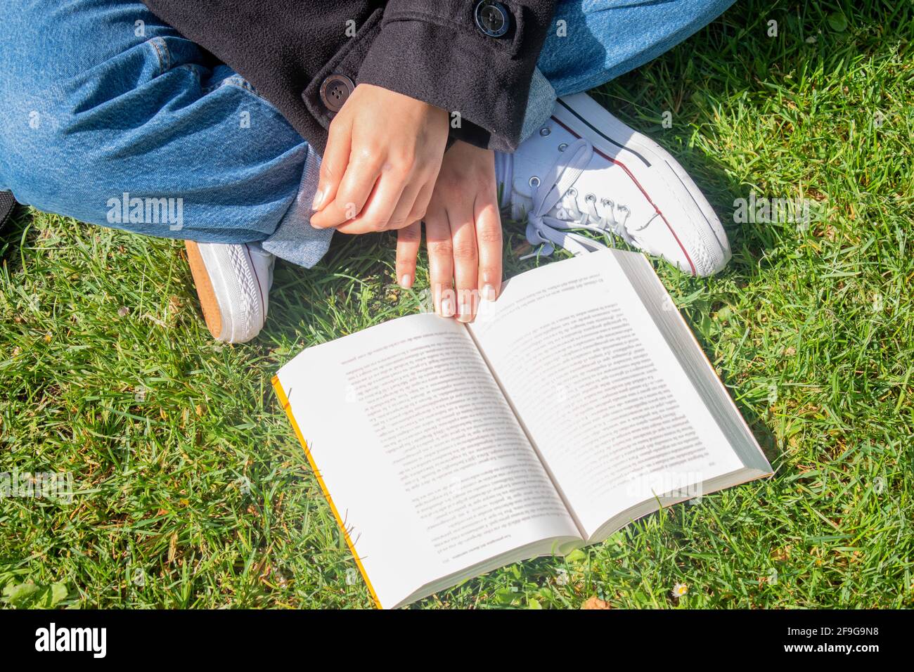 Draufsicht auf eine Person ohne Identität, die ein Buch auf dem Gras mit gekreuzten Beinen liest. Stockfoto