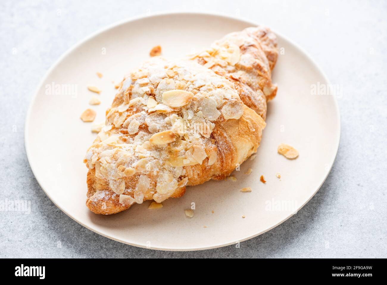 Mandelcroissant auf einem Teller, Nahaufnahme. Süßes französisches Gebäck gebackenes Croissant mit Mandelflocken und Puderzucker Stockfoto