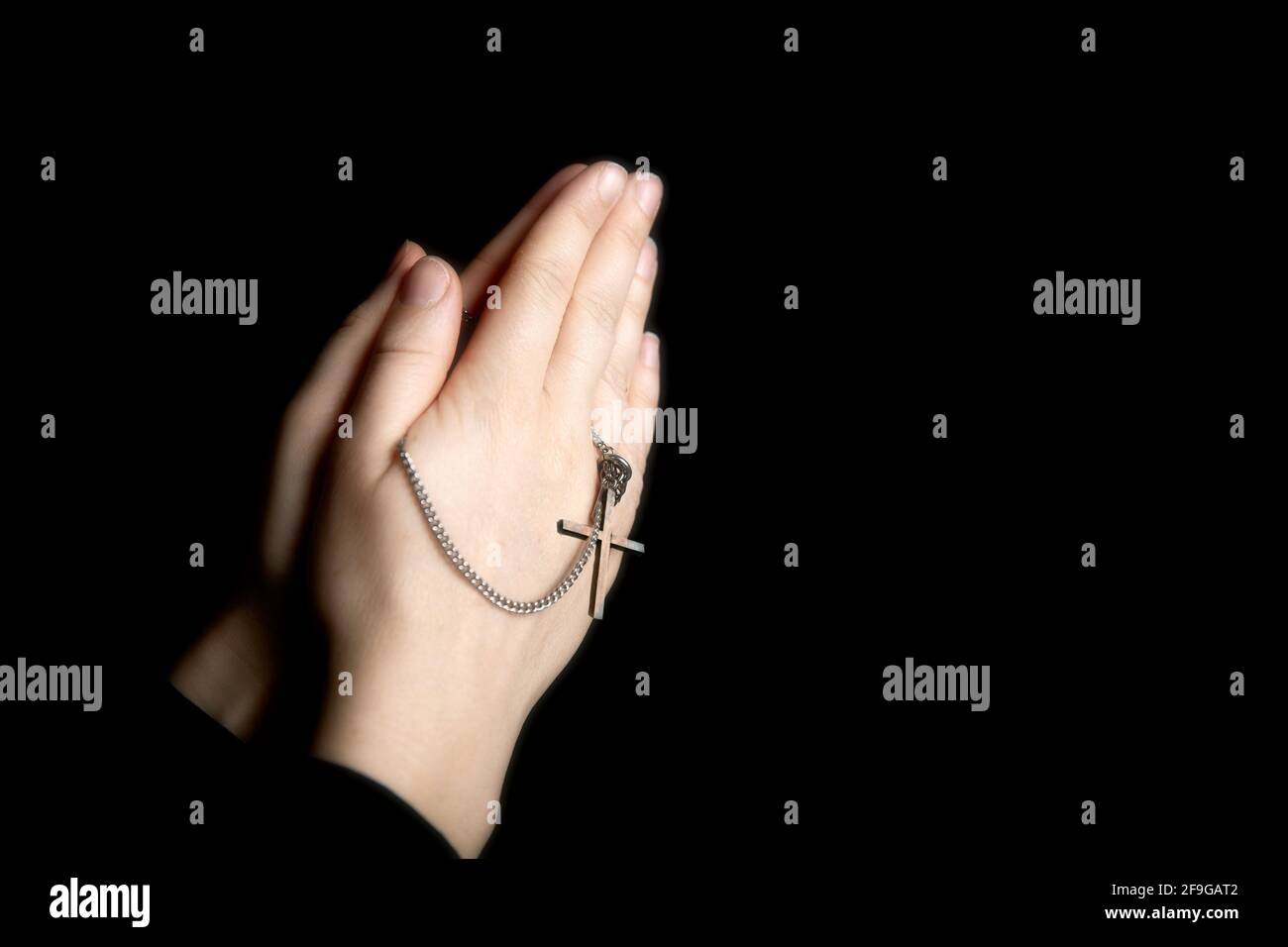 Betende Hände halten einen Rosenkranz, Closeup halten Halskette mit Kreuz, beten für gott im Dunkeln, religiöse christliche Symbol Stockfoto