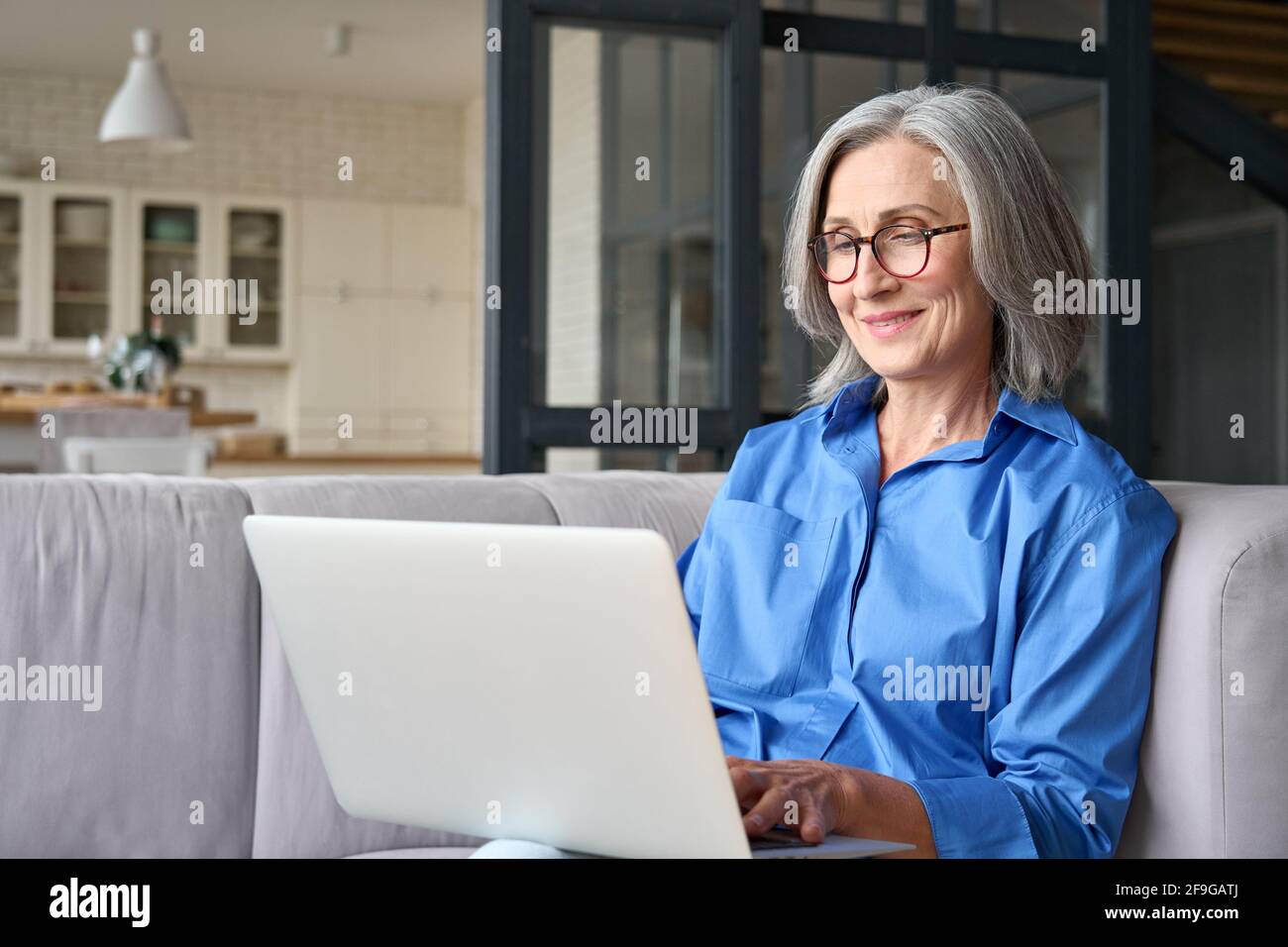 Ältere 60-Mann-Frau, die zu Hause Computertechnik verwendet und auf dem Sofa sitzt. Stockfoto