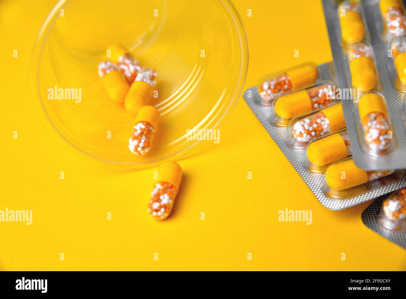 Kapseln in einer Blister und einem Glas. Medizinische Tabletten, Vitamine in einem Granulat, in gelben Kapseln auf einem gelben Hintergrund. Blur als kreative Idee der A Stockfoto
