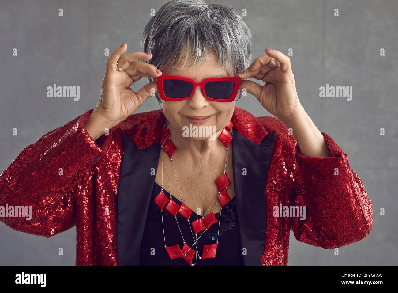 Porträt von lustigen glücklich zuversichtlich, ältere Frau in roten Pailletten Outfit und coole Sonnenbrille Stockfoto