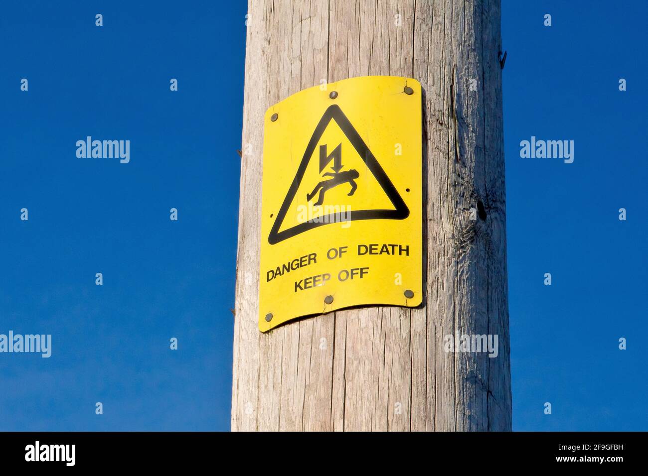 Nahaufnahme eines gelben UK-Warnschildes, das an einem hölzernen Strompylon angebracht ist, und warnt vor einer Todesgefahr durch Stromschlag und zur Abmeldung. Stockfoto