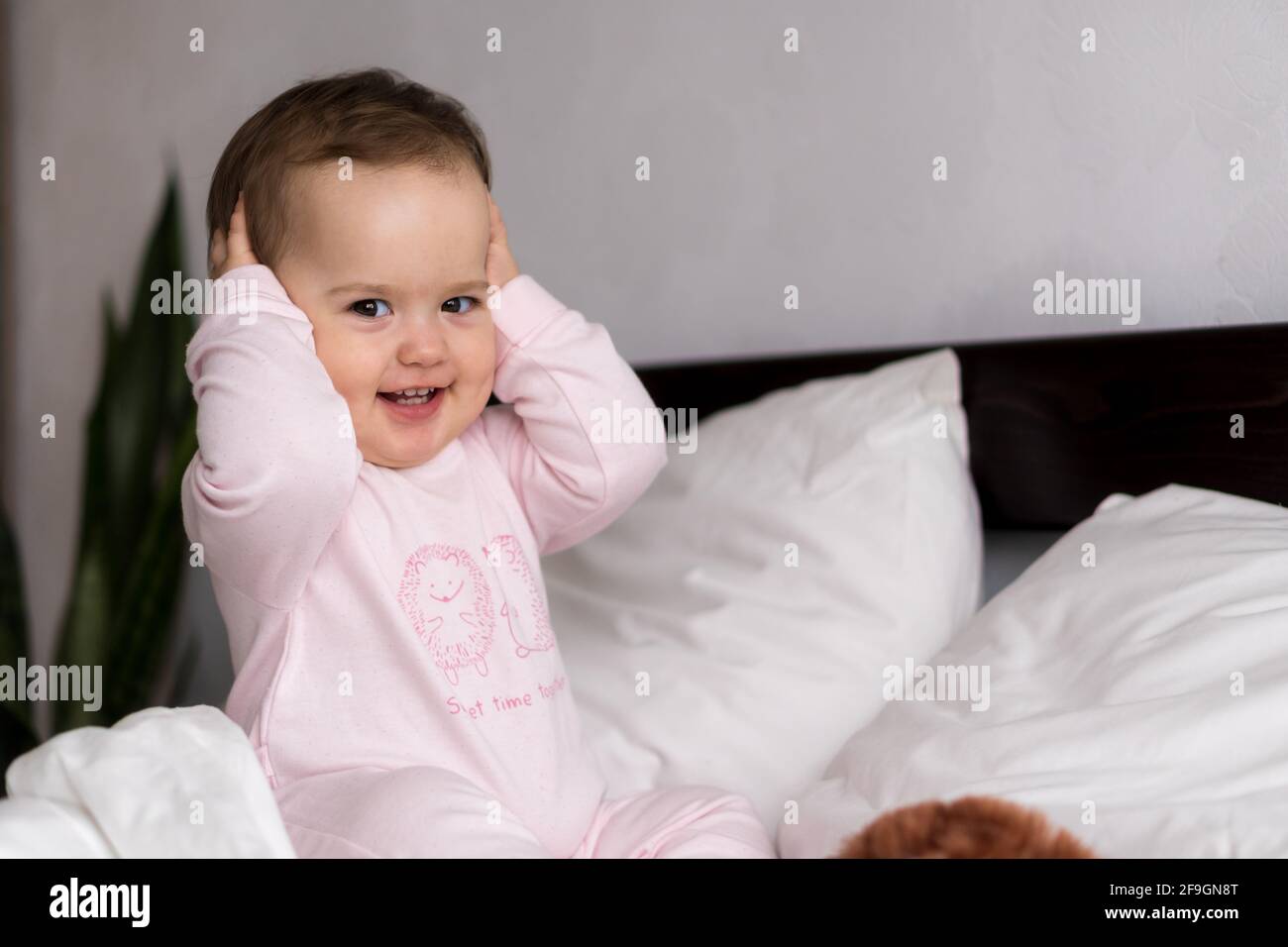Authentische Porträt kaukasischen kleinen Säugling mollig Baby Mädchen oder Jungen In rosa verschlammen beim Aufwachen Blick auf die Kamera lächelnd niedlich Und Grimassen im weißen Bett Stockfoto
