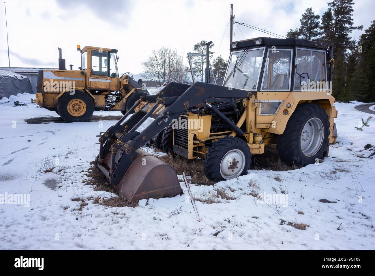 Zwei alte rostige Ladertraktoren stehen auf einem Schneefeld - klein und groß, Winterzeit. Stockfoto