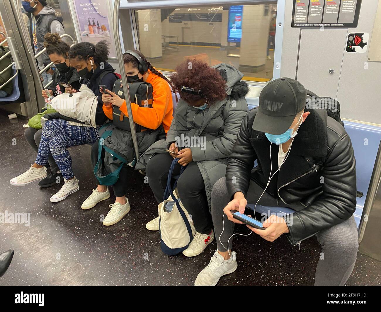 Masken wie Handys sind jetzt ein regelmäßiger Bestandteil der U-Bahn-Züge in New York City zu fahren, da die Covid-19-Pandemie in ihr zweites Jahr geht. Fahrer scheinen sich nicht zu sehr um soziale Distanz zu sorgen. Stockfoto