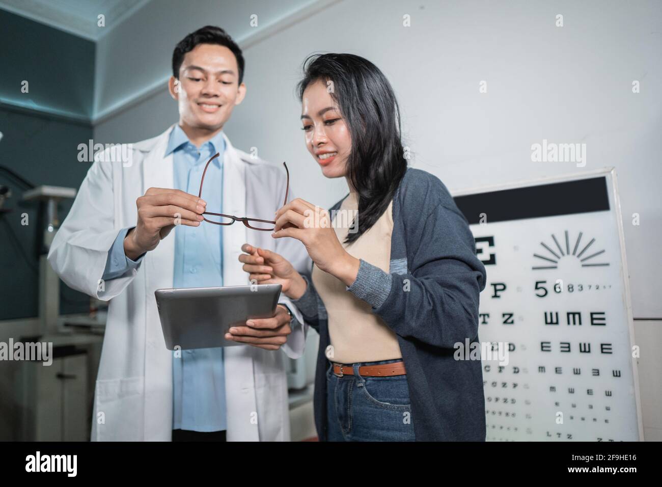 Ein männlicher Arzt gibt der Patientin die Ergebnisse Der Analyse und der Darstellung der empfohlenen Gläser Nach der Überprüfung Stockfoto
