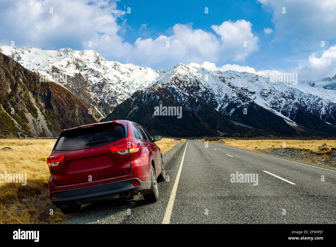 Rotes SUV-Auto am Straßenrand, Hintergrund groß und hoch Berge im Winter, trockenes Gras wird gelb in blauen Himmel und Wolken am Tag in Mount c Stockfoto