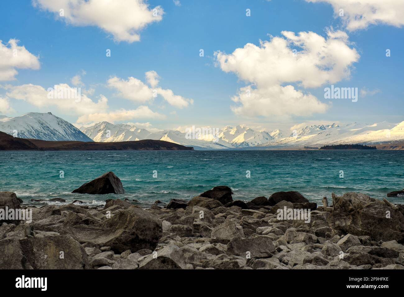 Felsen im türkisfarbenen Wasser, Wellen im Lake Tekapo, Hintergrund sind die Mount Cook Mountains. An einem schönen bewölkten Tag auf der Südinsel Neuseelands. Stockfoto