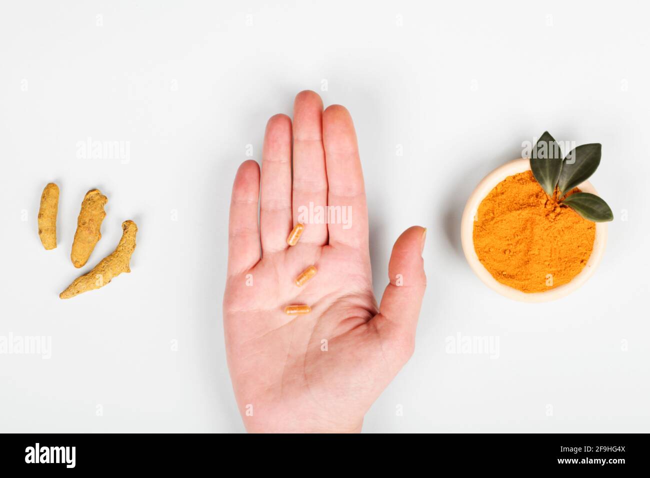 Health Care Lifestyle-Konzept. Kurkuma Longa oder Kurkuma Pulver in Schale mit grünem Blatt, Wurzel und Hand mit Pillen auf blauem Hintergrund. Draufsicht Stockfoto