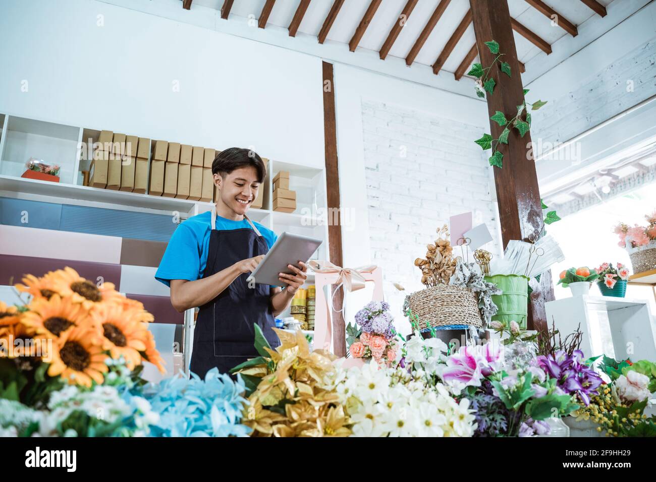 Glücklicher junger Mann Unternehmer, der in einem Blumengeschäft mit Schürze arbeitet Lächelnd Stockfoto