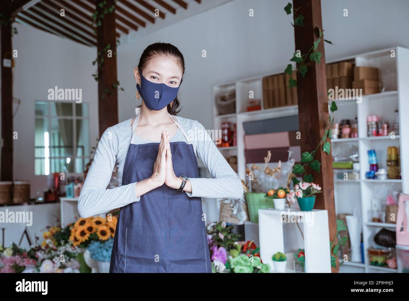 Junge Managerin trägt Schürze und Gesichtsmaske Floristin stehend Grußansage posieren Stockfoto