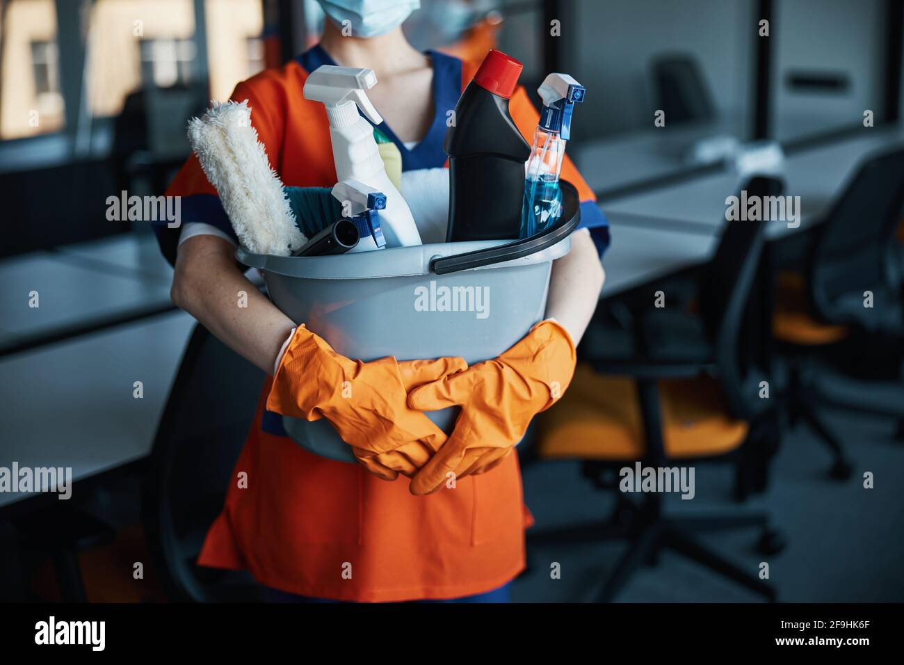 Reinigungskraft in einer Gesichtsmaske, die ihre Reinigungsprodukte zeigt Stockfoto