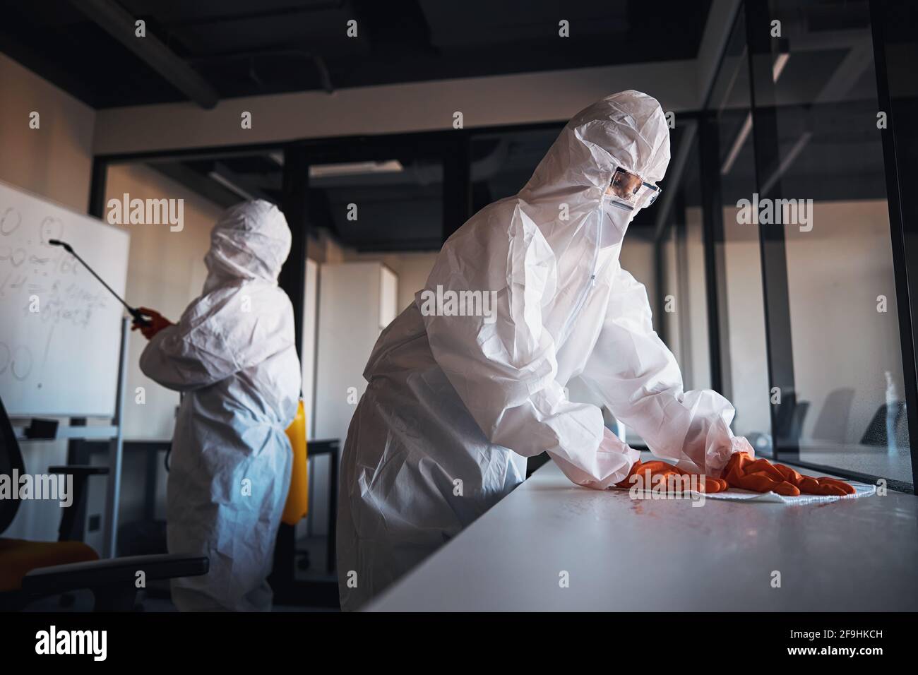 Reinigungspersonal in Schutzkleidung, die die Büroarbeitsplätze desinfiziert Stockfoto