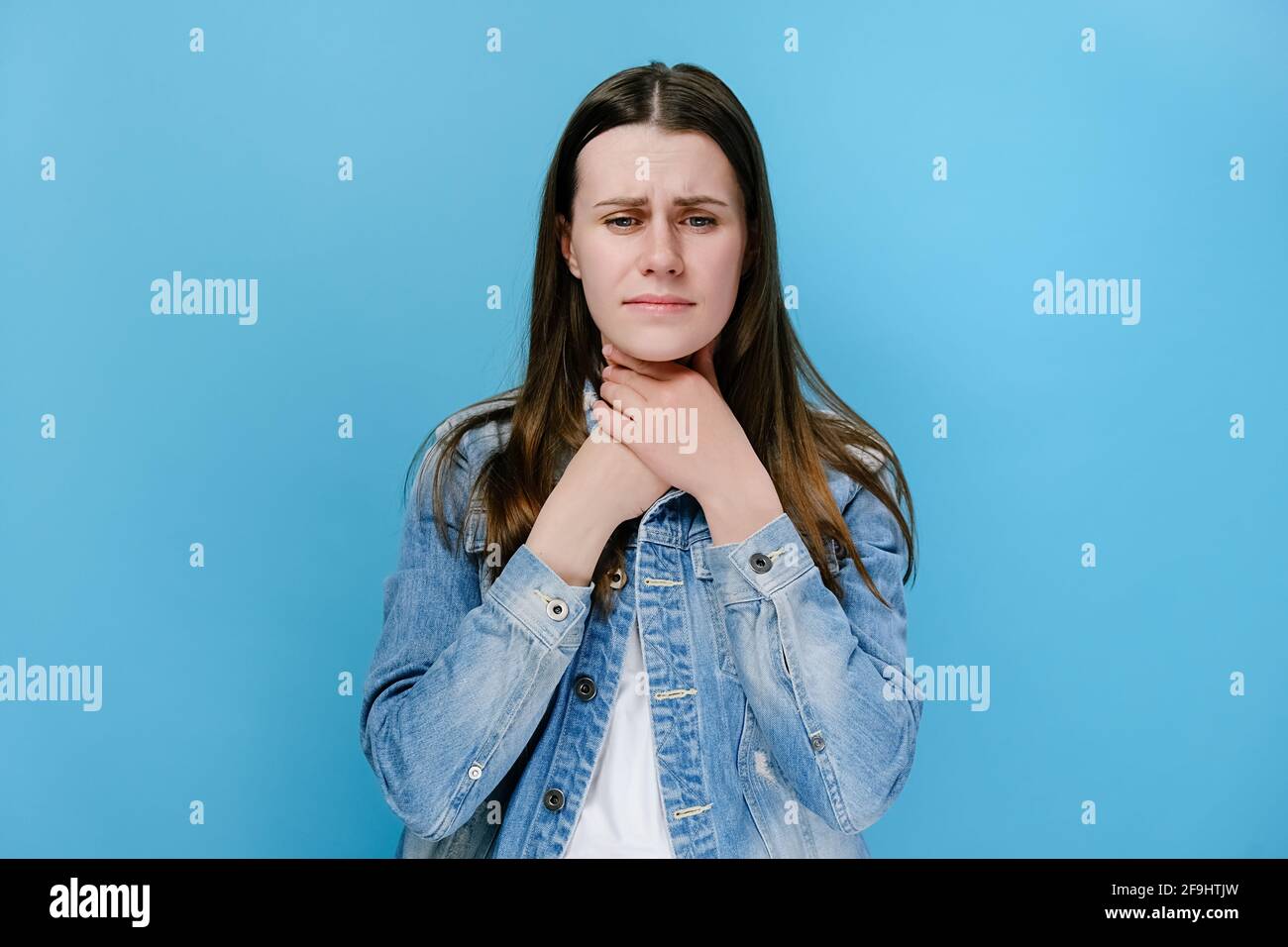 Unglücklich kranke junge Frau berührt den Hals, leidet an Halsschmerzen, hat Asthmaanfall, würgt und grinst Gesicht, isoliert auf blauem Studiohintergrund Stockfoto