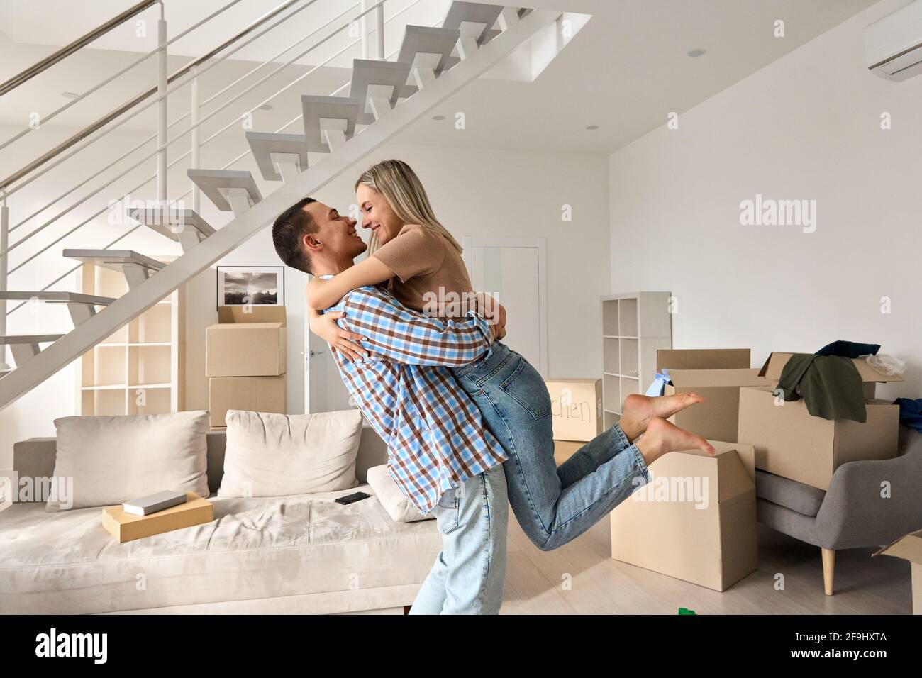 Glückliches junges Paar zum ersten Mal Hausbesitzer umarmten im Wohnzimmer am Umzugstag. Stockfoto