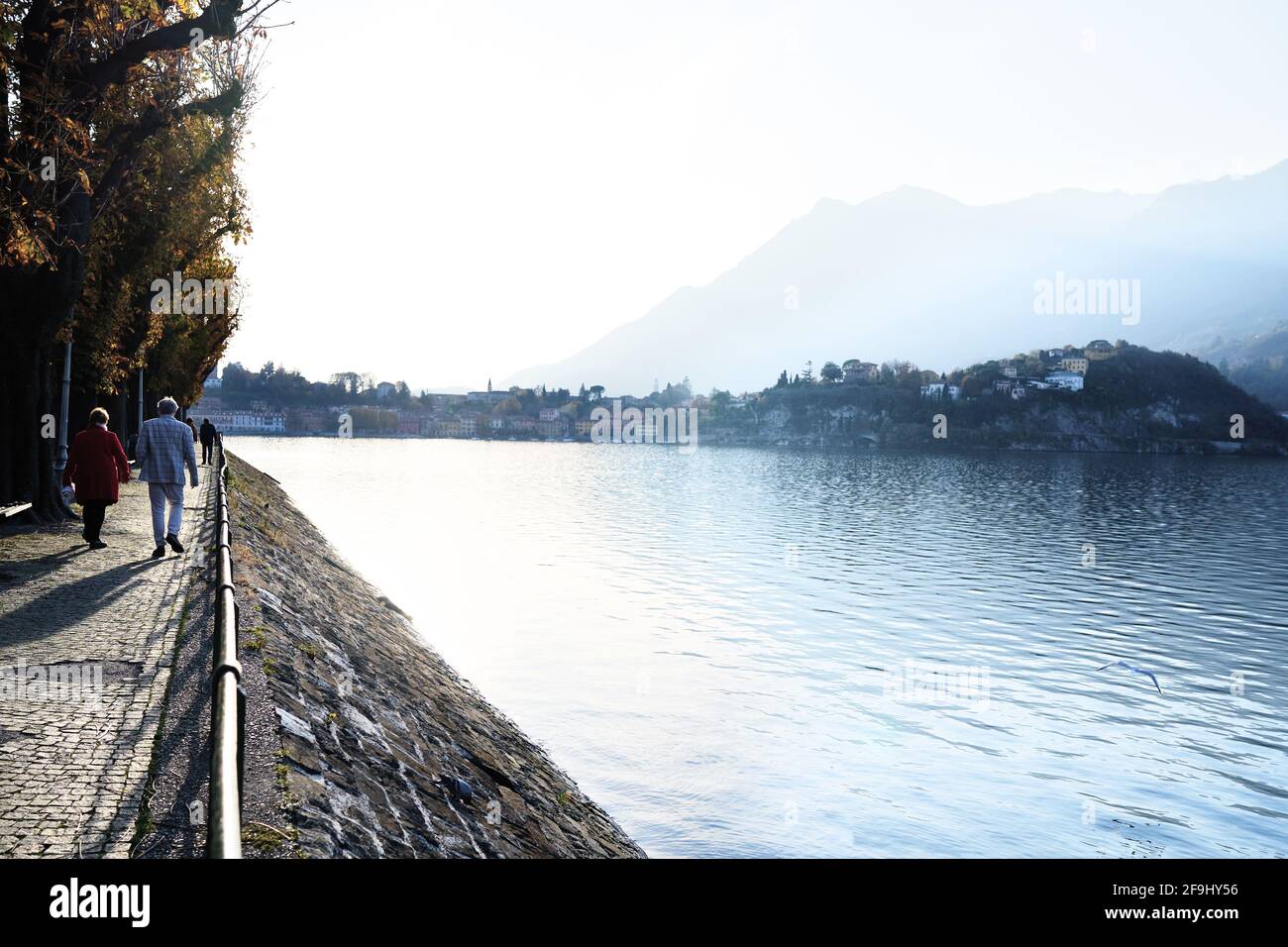 Ältere ältere Paare, die gemeinsam im Freien entlang des italienischen Bergseeregivteils Como spazieren gehen. Lecco, Italien - 11. November 2020 Stockfoto