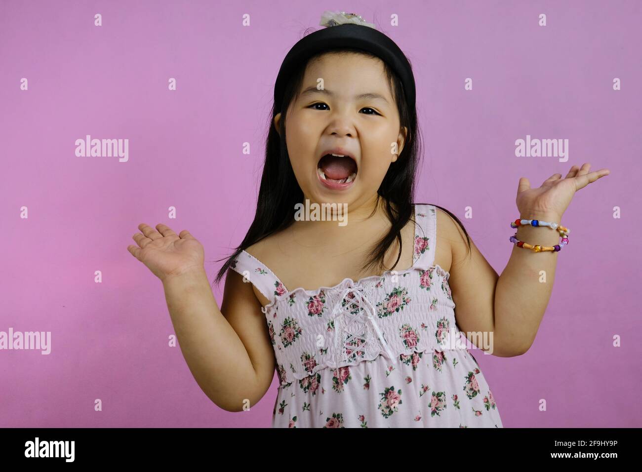 Ein süßes junges molliges asiatisches Mädchen, das sich aufgeregt und schreiend fühlt, mit weit geöffnetem Mund und erhobenen Händen und rosa Hintergrund. Stockfoto
