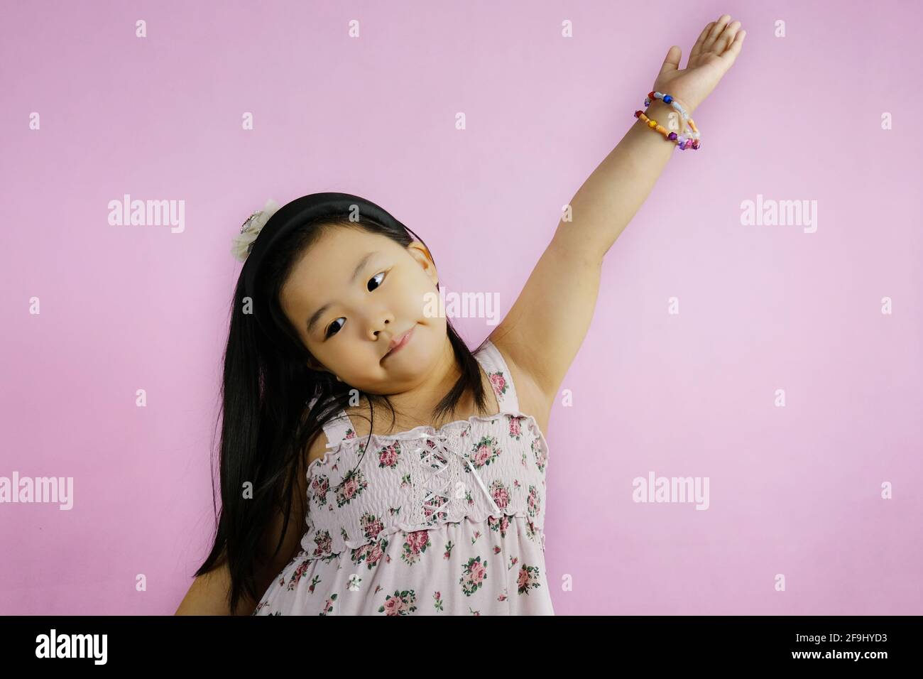 Ein süßes junges molliges asiatisches Mädchen hebt ihren Arm, um eine Frage von ihrem Lehrer mit Enthusiasmus und Zuversicht zu beantworten. Leuchtender rosafarbener Hintergrund. Stockfoto