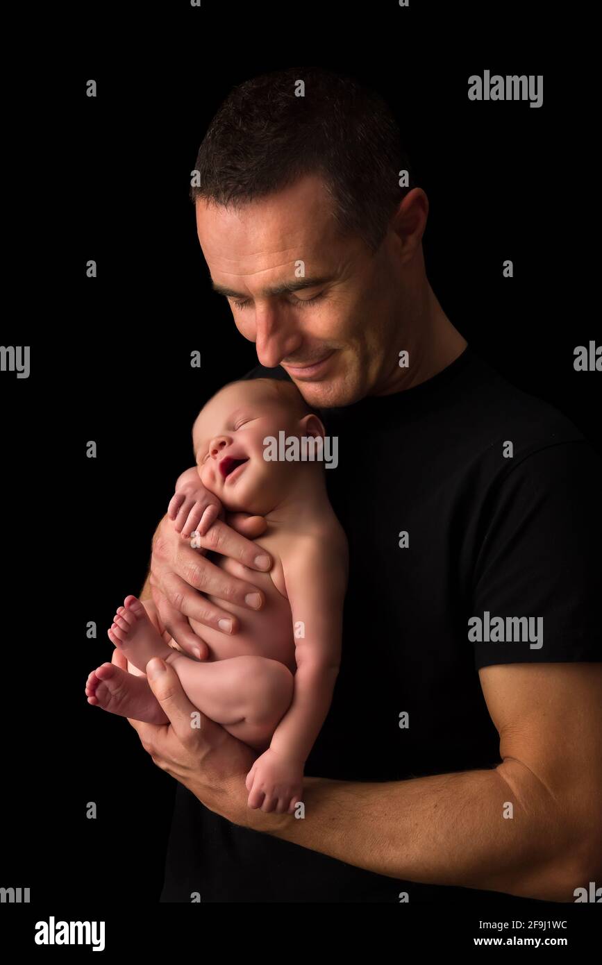 Junger Vater hält seinen 7 Tage alten neugeborenen Sohn Vor schwarzem Hintergrund Stockfoto