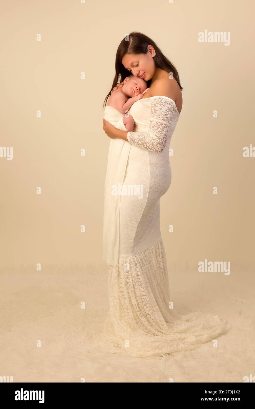 Schöne junge Mutter in einem weißen Spitzenkleid posiert mit Ihr 7 Tage alter neugeborener Sohn Stockfoto