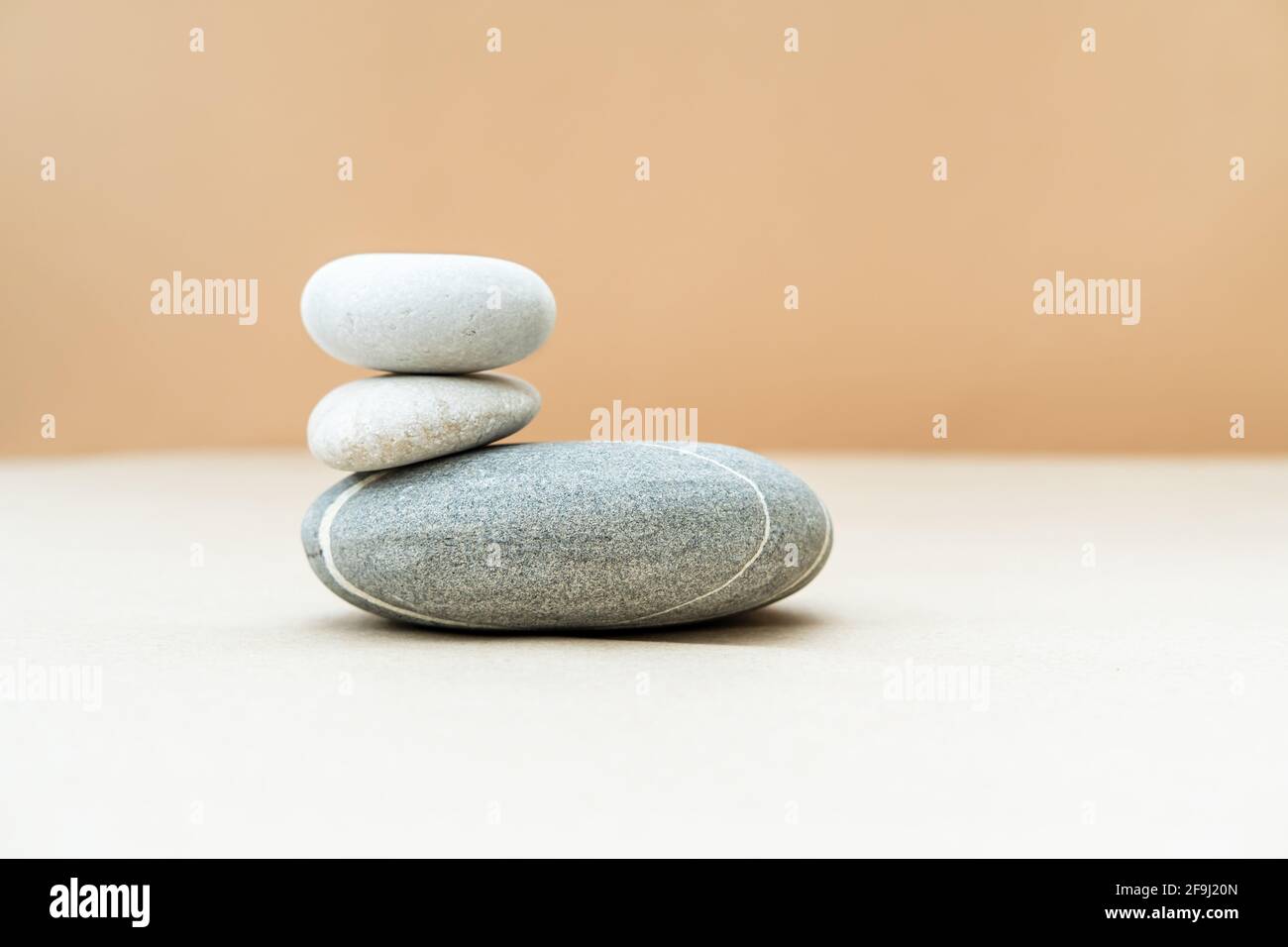 Haufen grauer Steine auf beigem Hintergrund. Einfache Balanciersteine, Einfachheit der Harmonie und des Gleichgewichts. Für Text platzieren. Stockfoto