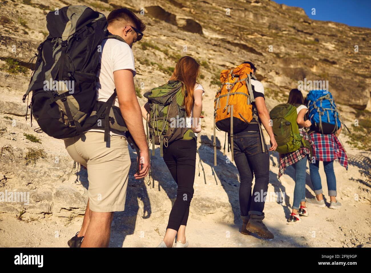 Eine Gruppe junger Wanderer mit Rucksäcken steigt an einem sonnigen Tag auf einen Bergpfad. Stockfoto