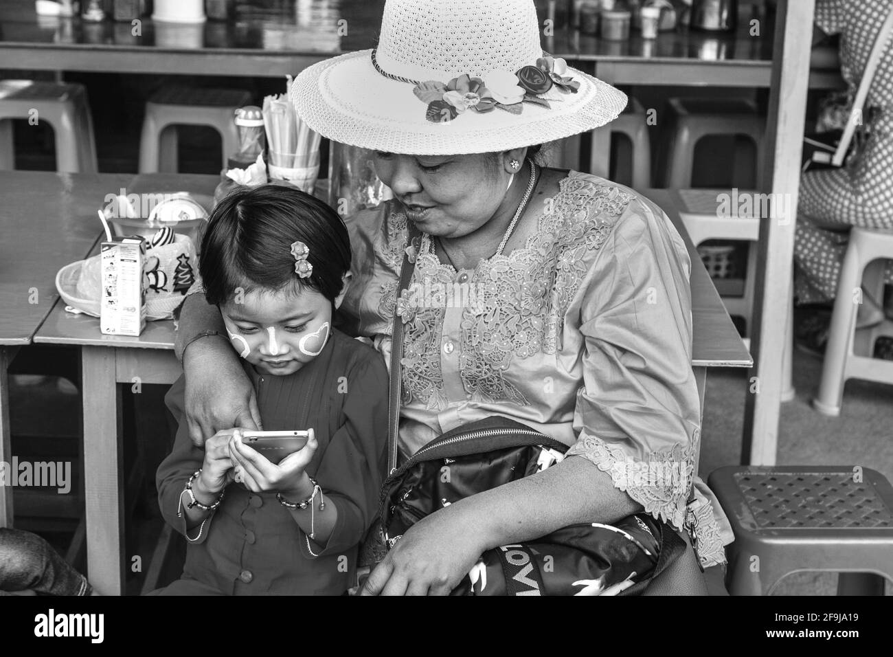 Eine burmesische Großmutter schaut mit Pride weiter, als ihre Enkelin ein Mobiltelefon (Mobiltelefon), Pindaya, Shan State, Myanmar, verwendet. Stockfoto