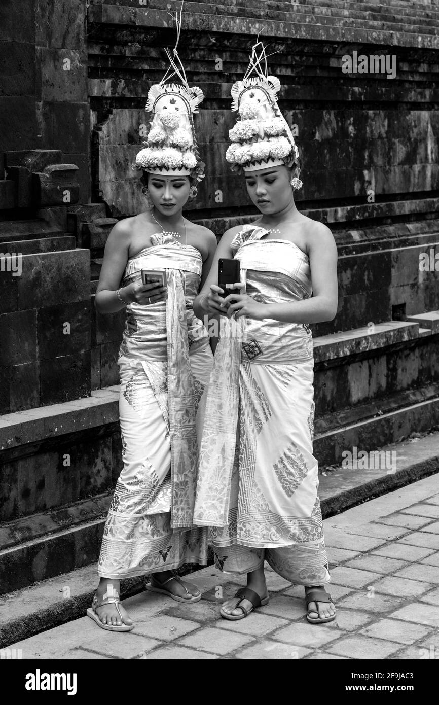 Zwei junge balinesische Hindu-Weibchen, die ein Handy (Handy) bei der Zeremonie Batara Turun Kabeh, Besakih-Tempel, Bali, Indonesien, ansehen. Stockfoto