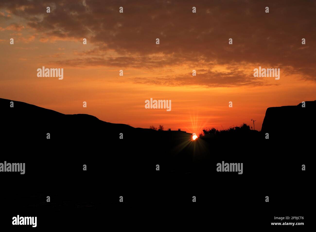 Erste Strahlen der Morgensonne hinter silhouettierten Felsen, mit orangefarbenem Himmel und Wolken. Helsinki, Finnland. 2021. Stockfoto