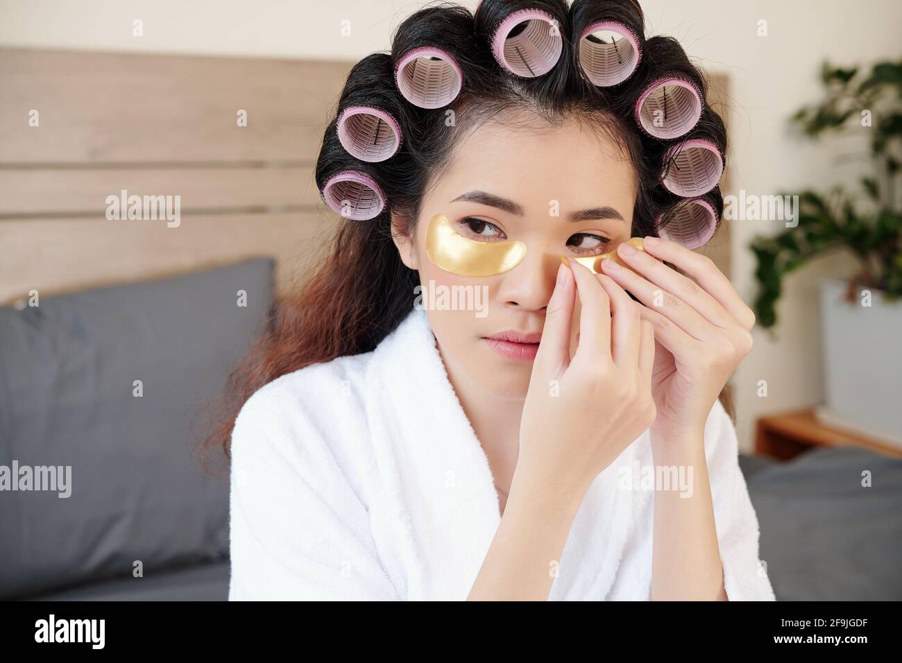 Schöne junge asiatische Frau mit Haarrollen Anwendung Patches unter Ihre Augen Stockfoto