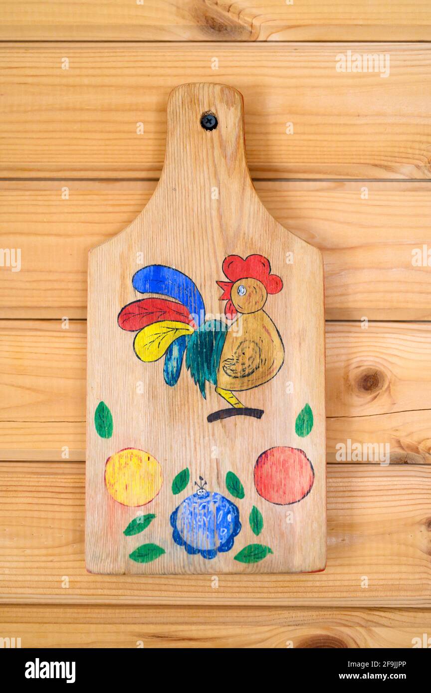 Altes Schneidebrett mit brennendem Holz und farbiger Zeichnung hängt ein  Hahn auf einem Nagel an der hölzernen Dielenwand. diy-Kinderhandwerk  Stockfotografie - Alamy