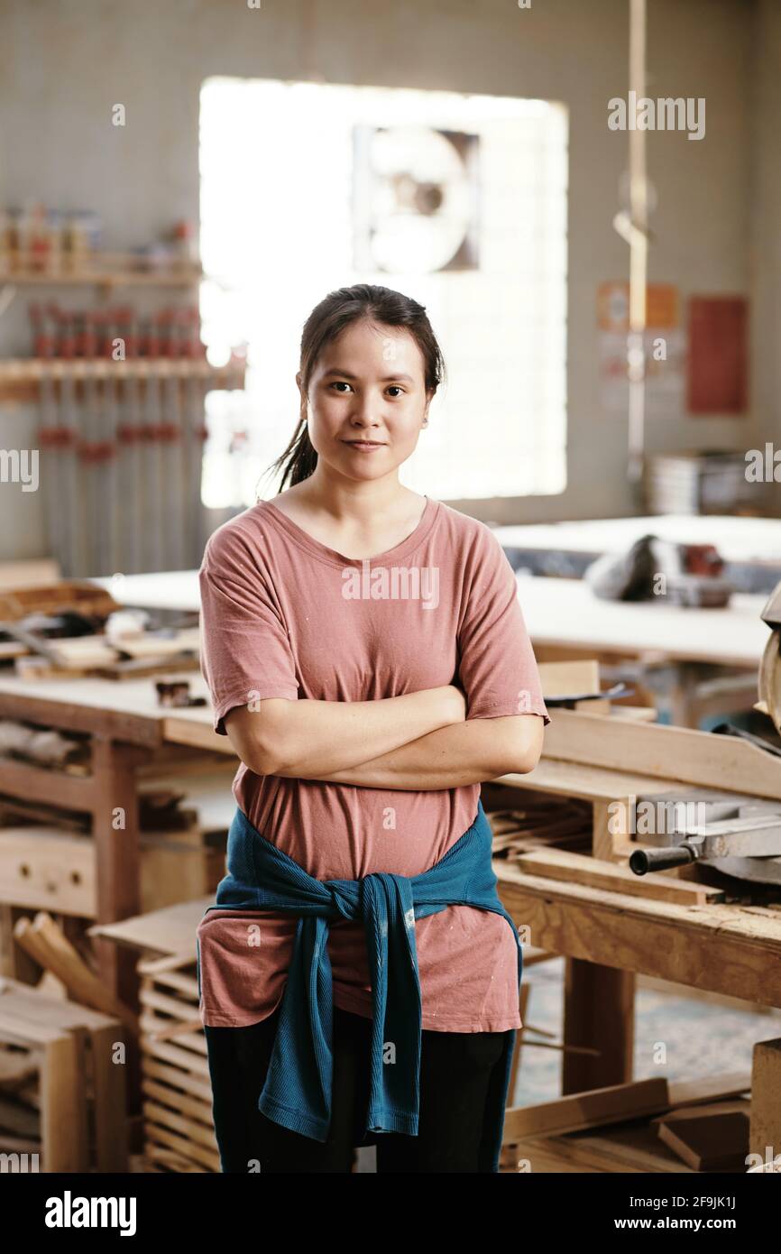 Porträt einer lächelnden, selbstbewussten jungen asiatischen Frau, die in Zimmerleuten steht Workshop, in dem sie arbeitet Stockfoto