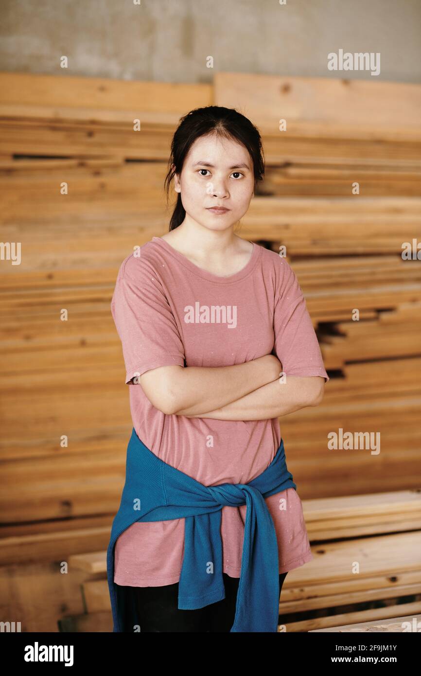 Porträt einer jungen selbstbewussten Tischlerin in legerer Kleidung im Stehen Mit gefalteten Armen und Blick auf die Kamera Stockfoto