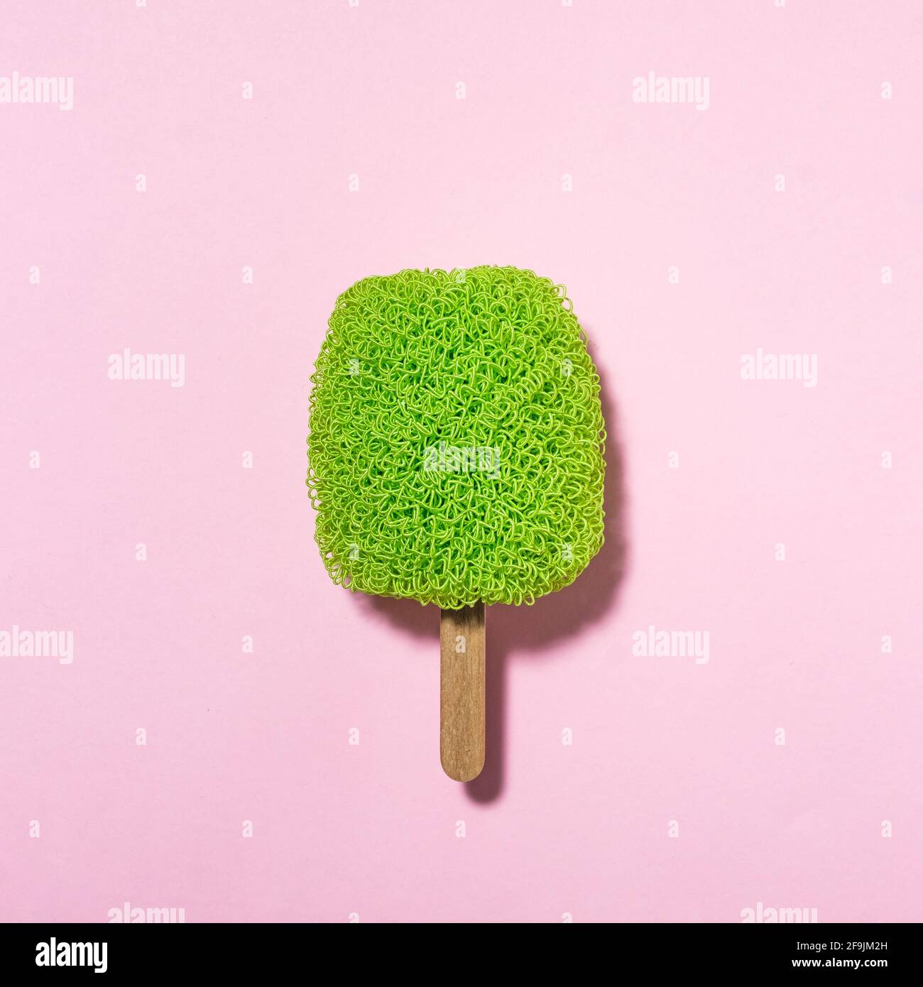 Waschschrubber auf einem Stock sieht aus wie Eis - Grünes Eis auf rosa Hintergrund mit trendigem Sonnenlicht - Minimal moderne Idee Stockfoto