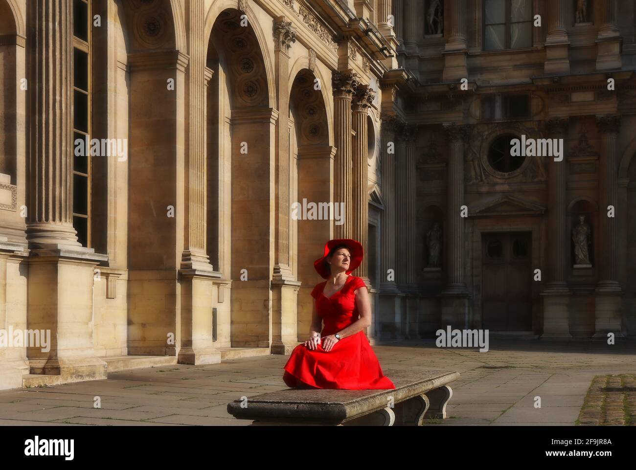 Paris, Frankreich, Louvre Innenhof des Louvre in Paris in Frankreich mit sitzender Frau mit rotem Kleid und rotem Hut Stockfoto
