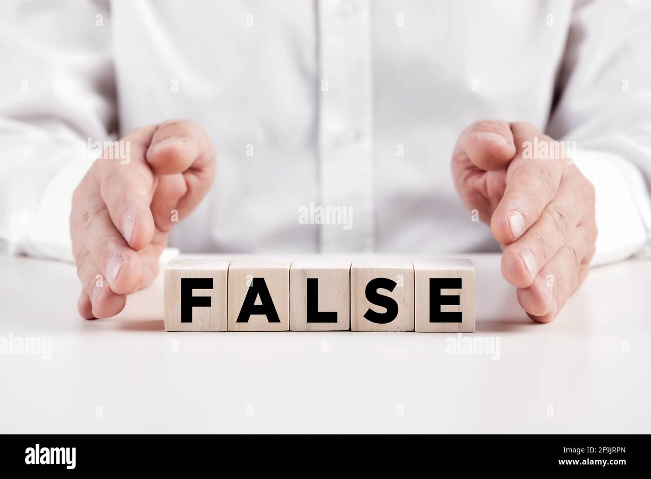 Die Hände des Geschäftsmannes decken die Holzwürfel mit dem Wort falsch ab. Irreführendes Informationskonzept. Stockfoto
