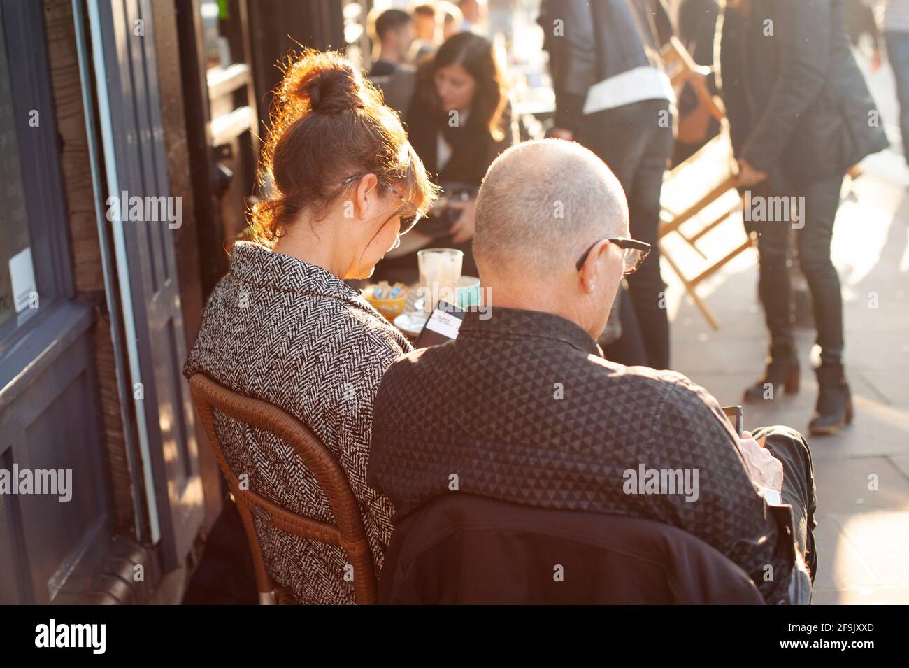 Rückansicht eines nicht verbundenen britischen Paares mittleren Alters, das vor einem Café seine Handys überprüfte. Broadway Market, E2, East London. November 2015 Stockfoto