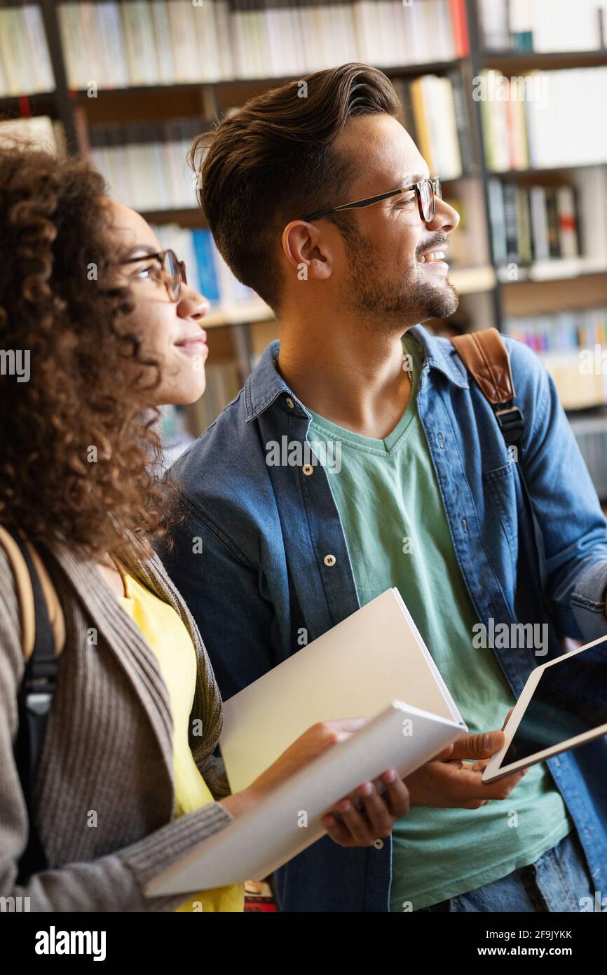 Gruppe glücklicher Studenten, die Bücher lesen und sich auf die Prüfung in der Bibliothek vorbereiten Stockfoto